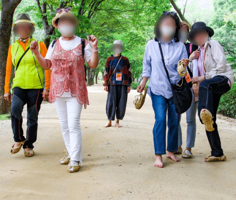 탐방객들이 신발과 짚신을 손에 든 채 문경새재의 부드러운 황토 흙길을 맨발로 걸어가고 있다. / 한국관광공사