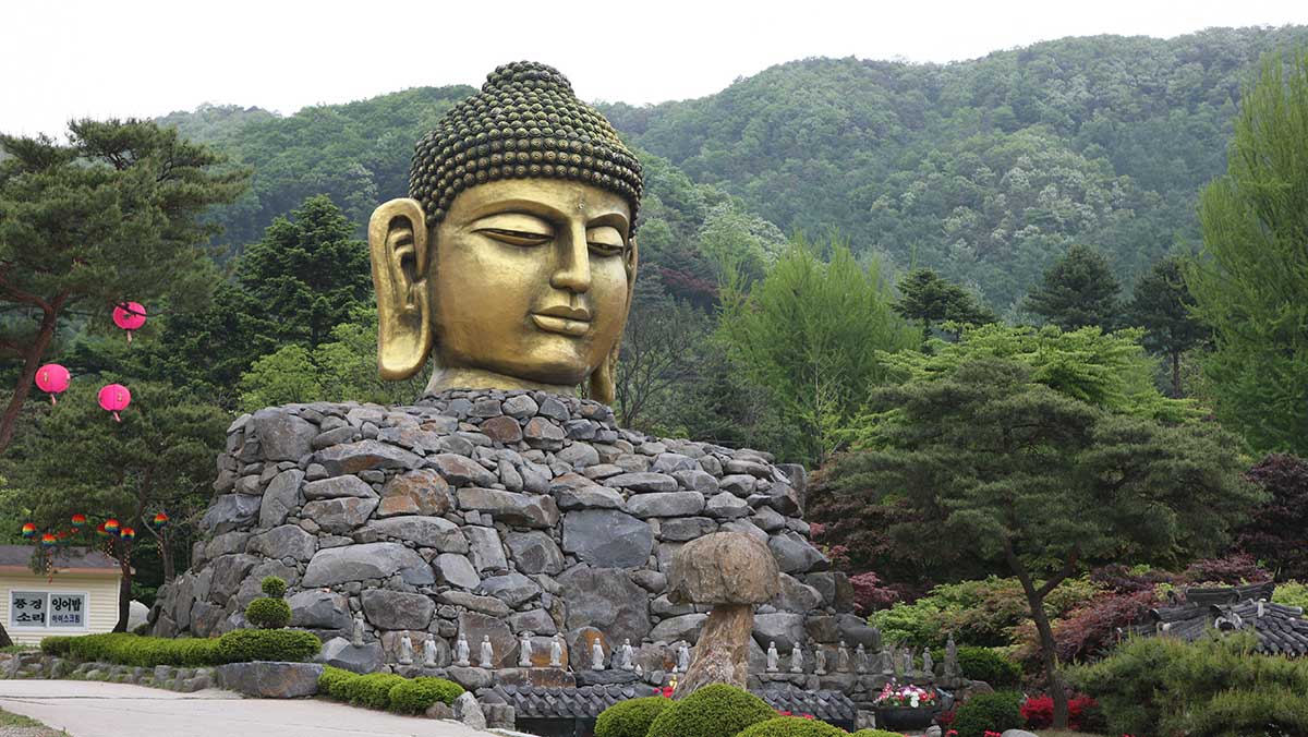 푸른 산을 배경으로 돌무더기 위에 웅장하게 자리한 와우정사 황금빛 불두의 모습. / 한국관광콘텐츠랩-김지호