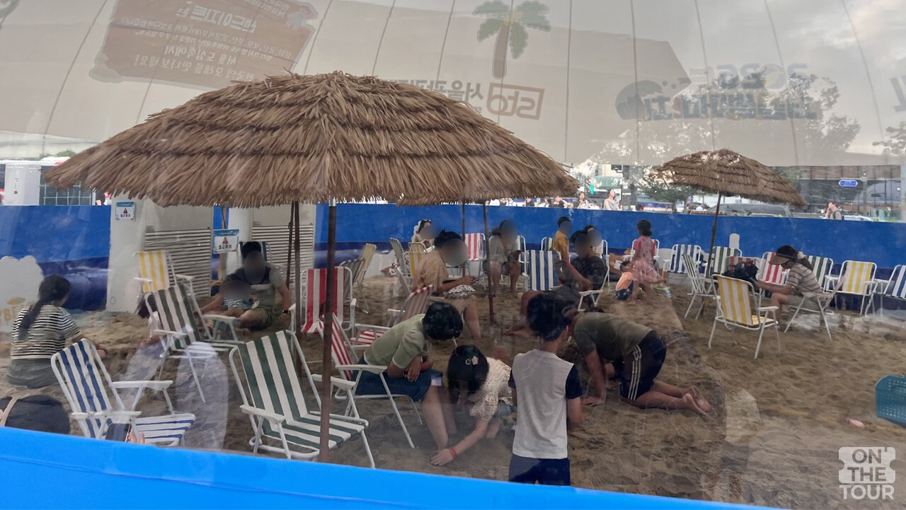 대형 돔 그늘 아래 파라솔과 의자를 갖춘 '샌드 아지트' 모래놀이터. / 온더투어