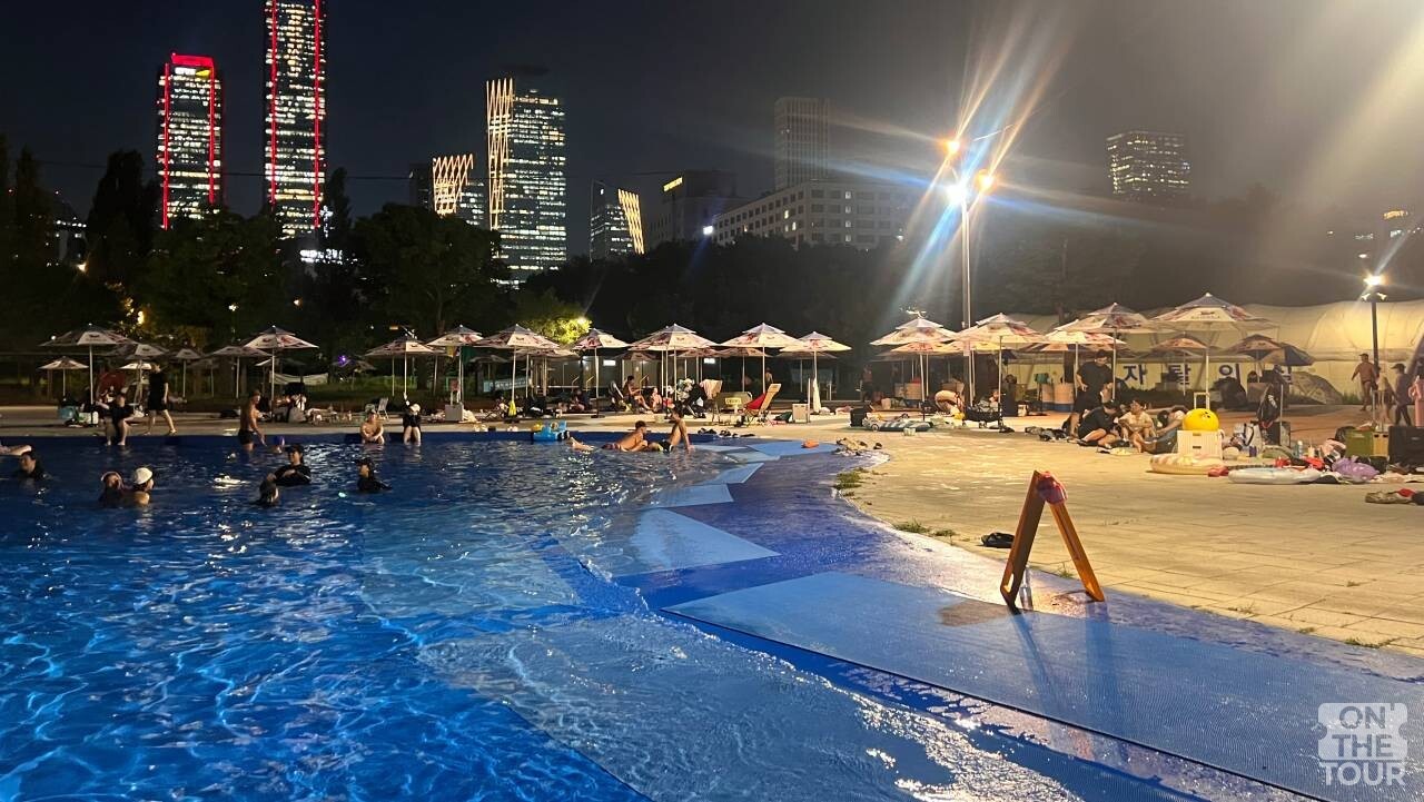 여의도 고층 빌딩 숲 야경과 파라솔 쉼터가 어우러진 여의도 한강수영장. / 온더투어
