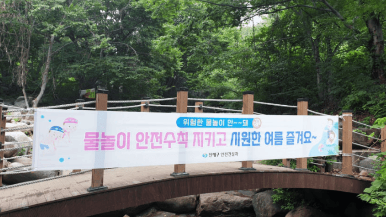 계곡 다리에 '물놀이 안전수칙' 현수막이 걸려 있어 안전한 물놀이를 안내하는 입구 풍경. / 창원시
