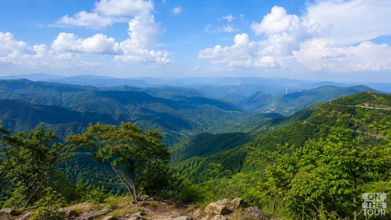 의령 한우산 별천지에서 내려다본 겹겹의 산 능선과 푸른 하늘. (AI 생성) / 온더투어