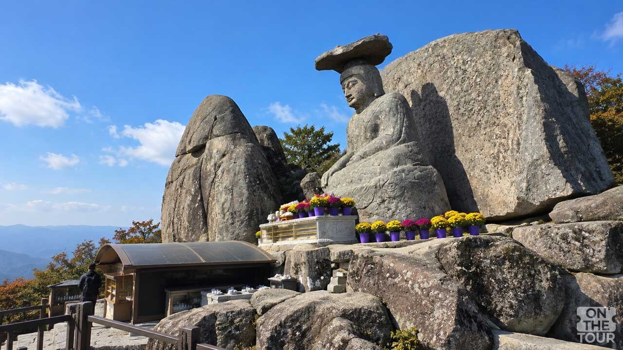 팔공산 관봉 정상 바위에 자리한 관봉석조여래좌상과 주변 암석이 맑은 가을 하늘 아래 펼쳐지고 있다. (AI 생성) / 온더투어
