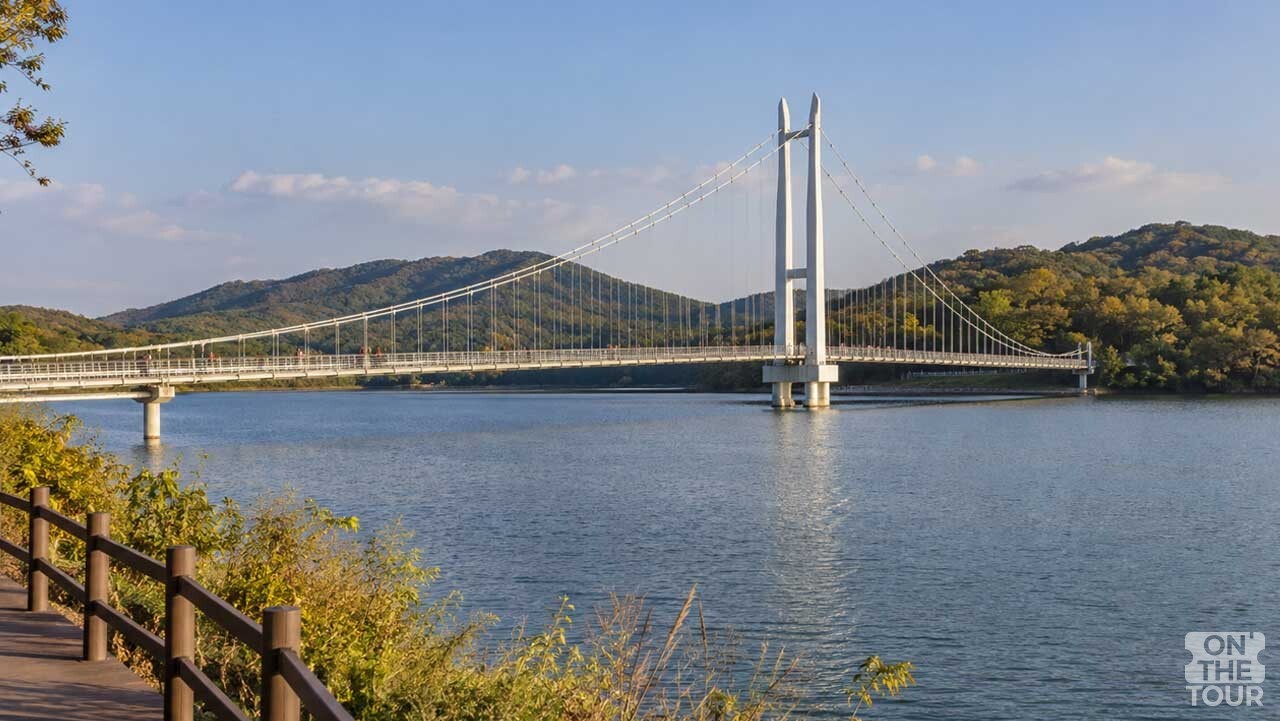 예산 예당호 수면 위로 길게 이어진 출렁다리와 흰색 주탑. (AI 생성) / 온더투어