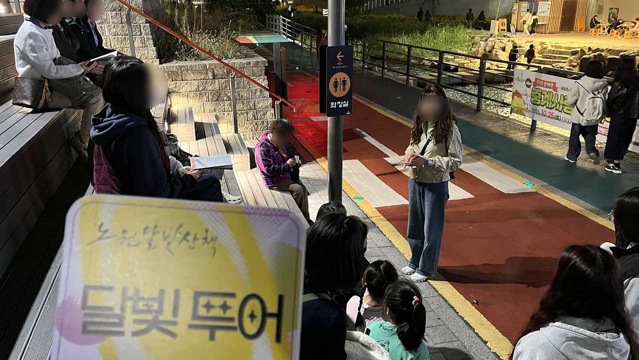 달빛투어 팻말을 든 안내자 앞에서 가족 관람객들이 해설을 듣고 있다. / 노원문화재단