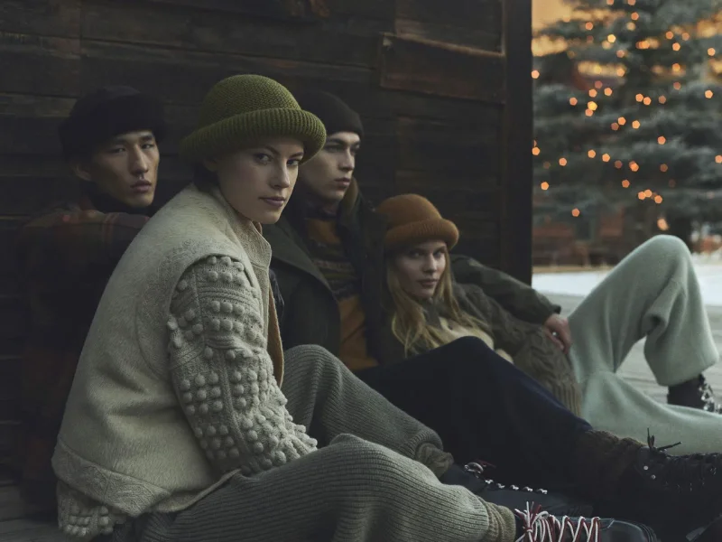 로로피아나 2026-27 가을/겨울 홀리데이 캠페인 이미지. 통나무 벽 앞에 앉은 모델들이 니트 모자와 타탄 코트 등을 착용했다. / 사진=로로피아나