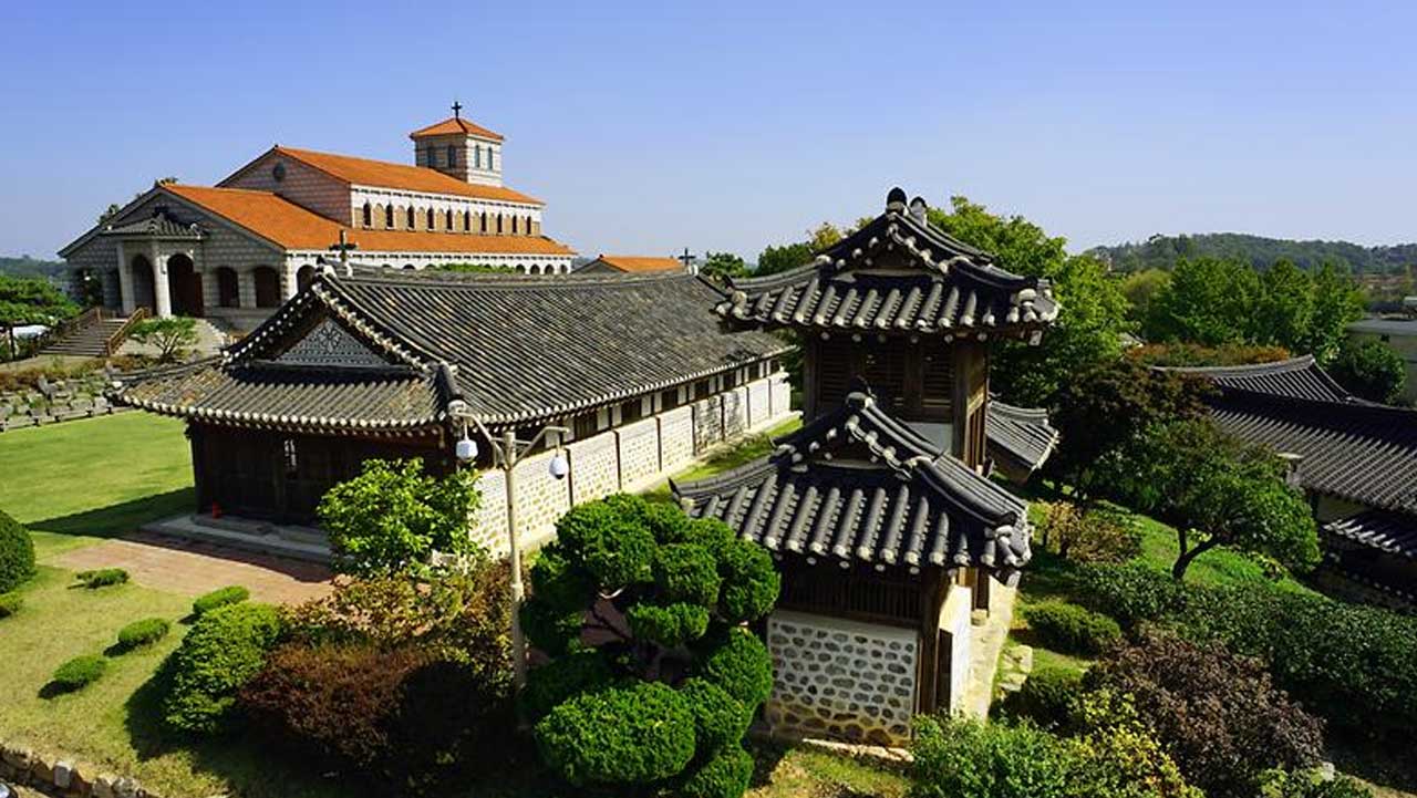 한옥 성당과 문루가 자리해 있고, 뒤쪽으로 붉은 기와지붕의 서양식 성당이 서 있다. / 강화군 문화관광