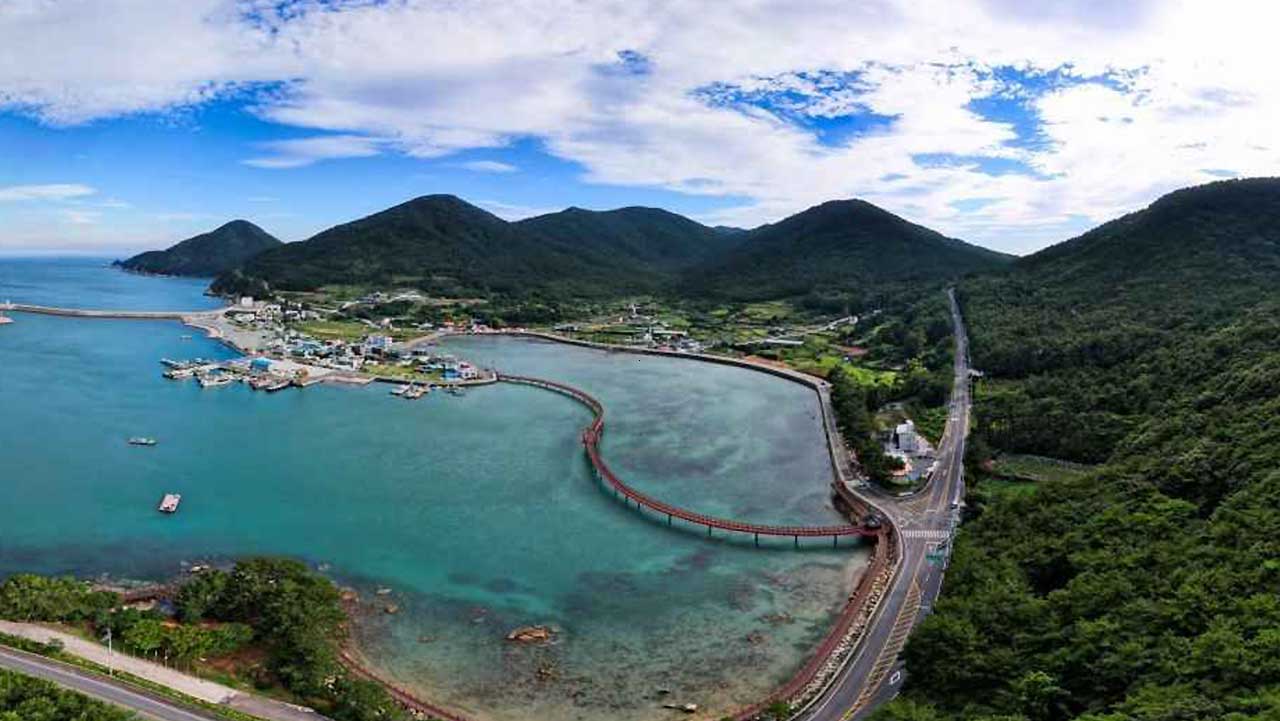산자락과 마을 사이 만 안쪽으로 붉은 보행로가 굽이쳐 지나간다. / ⓒ한국관광콘텐츠랩-라이브스튜디오