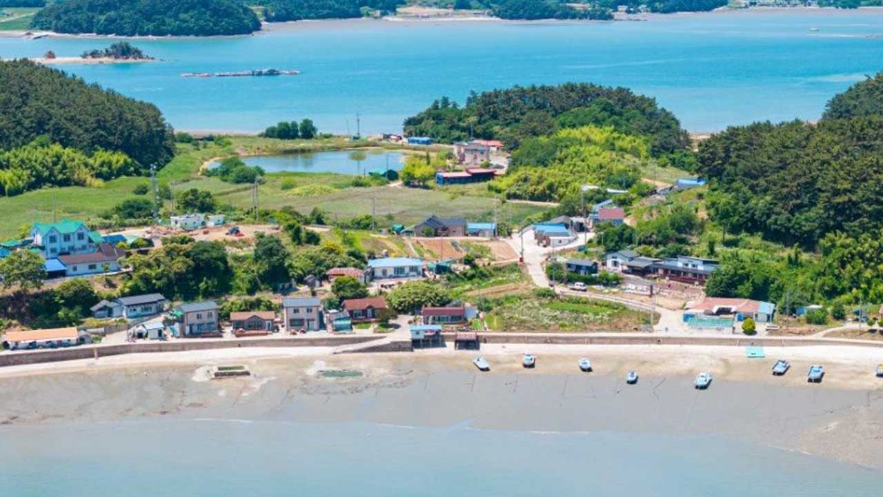 서산 고파도 마을 앞 갯벌에 작은 배들이 놓여 있고, 뒤로 집들과 연못이 보인다. / 한국관광콘텐츠랩