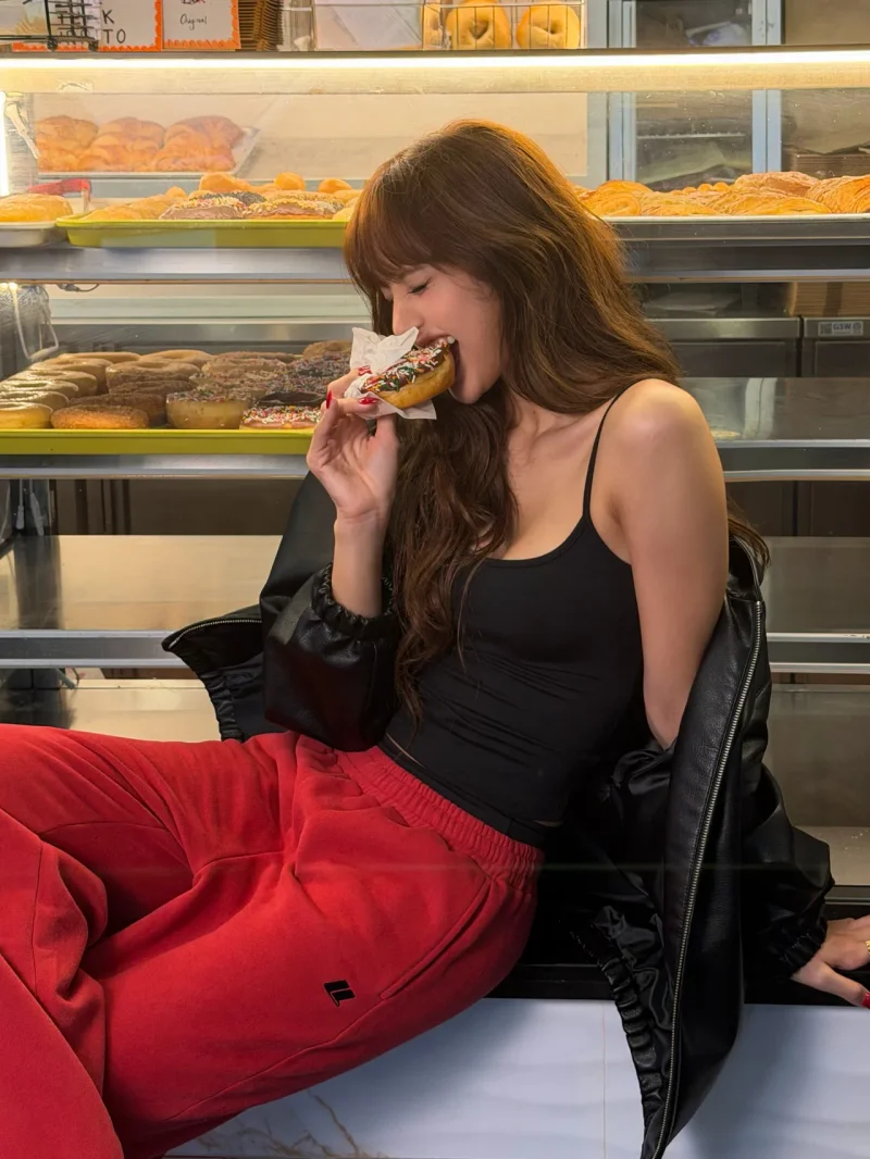 리사가 블랙 캐미솔에 레드 스웨트팬츠를 입고 레더 재킷을 어깨에 걸친 채 도넛을 먹고 있다. / 사진=리사 인스타그램